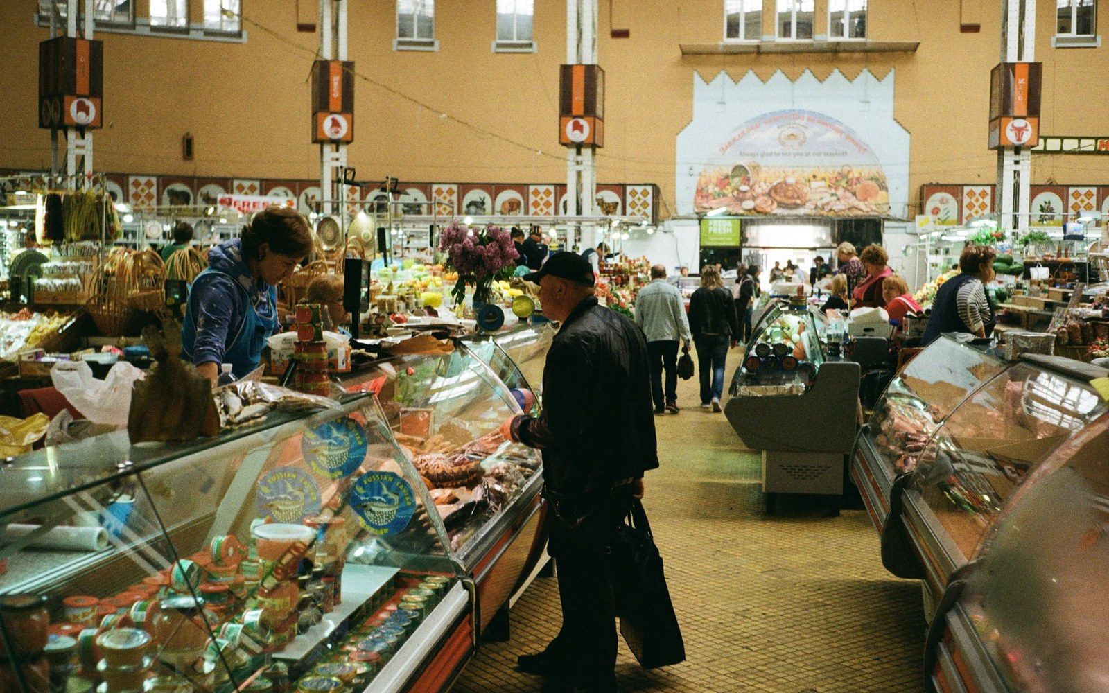 A Findlay Market vendor behind a produce stall, hands visible arranging goods, market hall ironwork behind