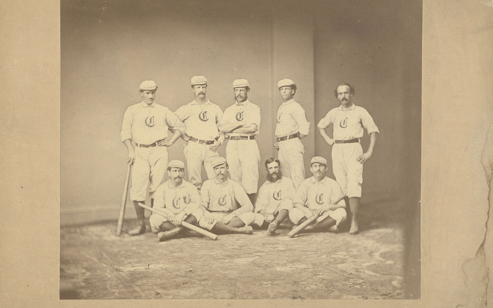 Vintage studio portrait of a mustached baseball team in matching caps and jerseys with bats