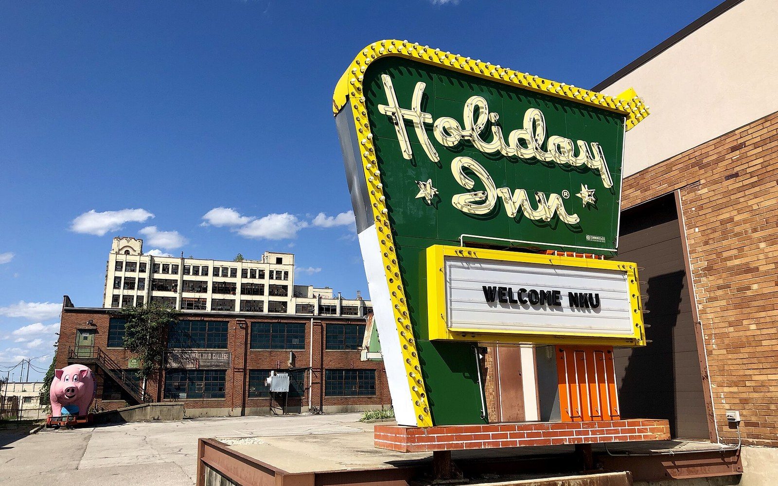 A vintage Holiday Inn sign with a marquee reading "Welcome NKU" beside old brick buildings