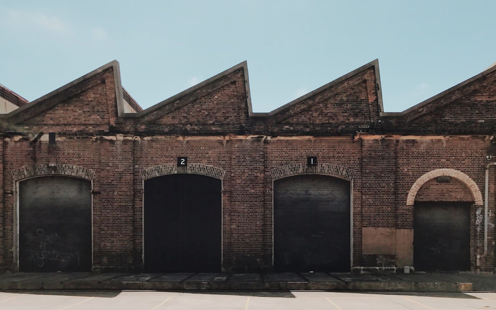 Sawtooth-roofed brick warehouse with arched loading bay doors numbered one and two