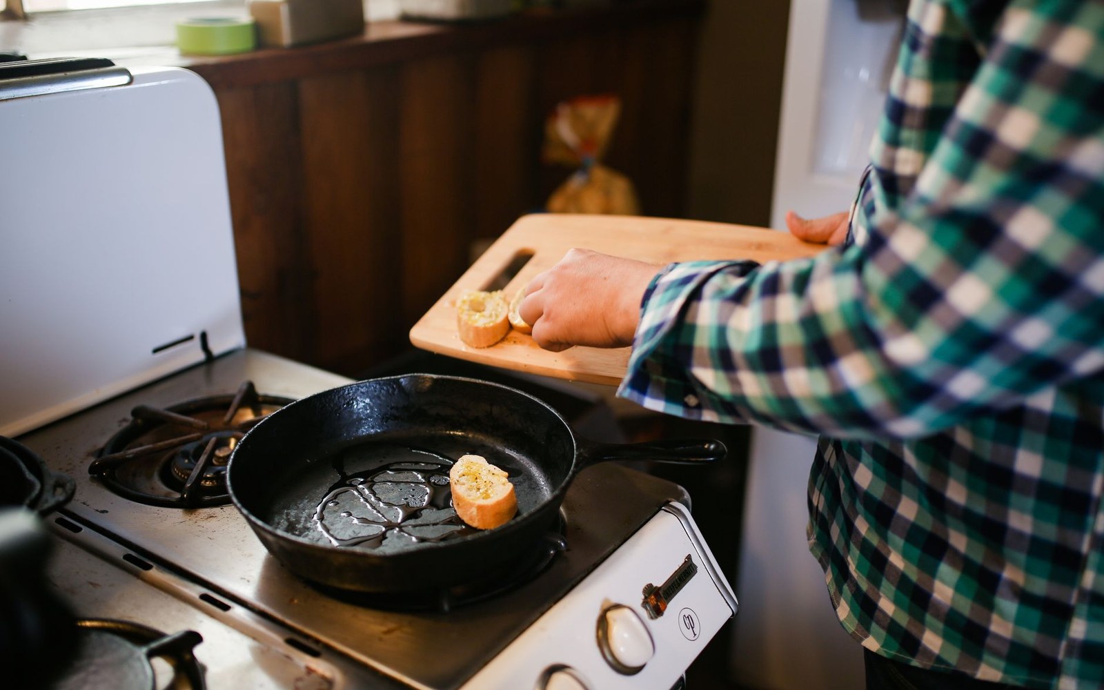 Person slides sliced goetta from a cutting board into a cast-iron skillet on a stove