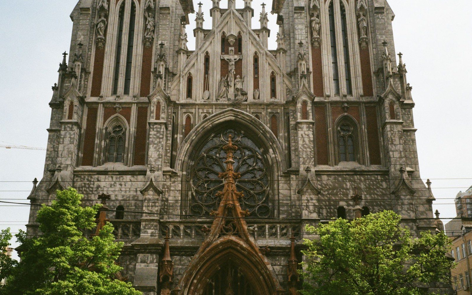 Gothic revival church facade with a rose window and twin spires above green trees