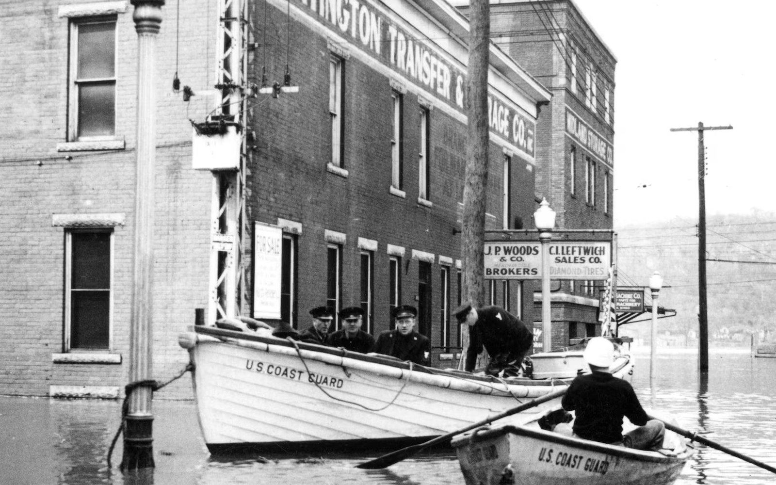 Coast Guard boats navigate a flooded street lined with brick storefronts and streetlights