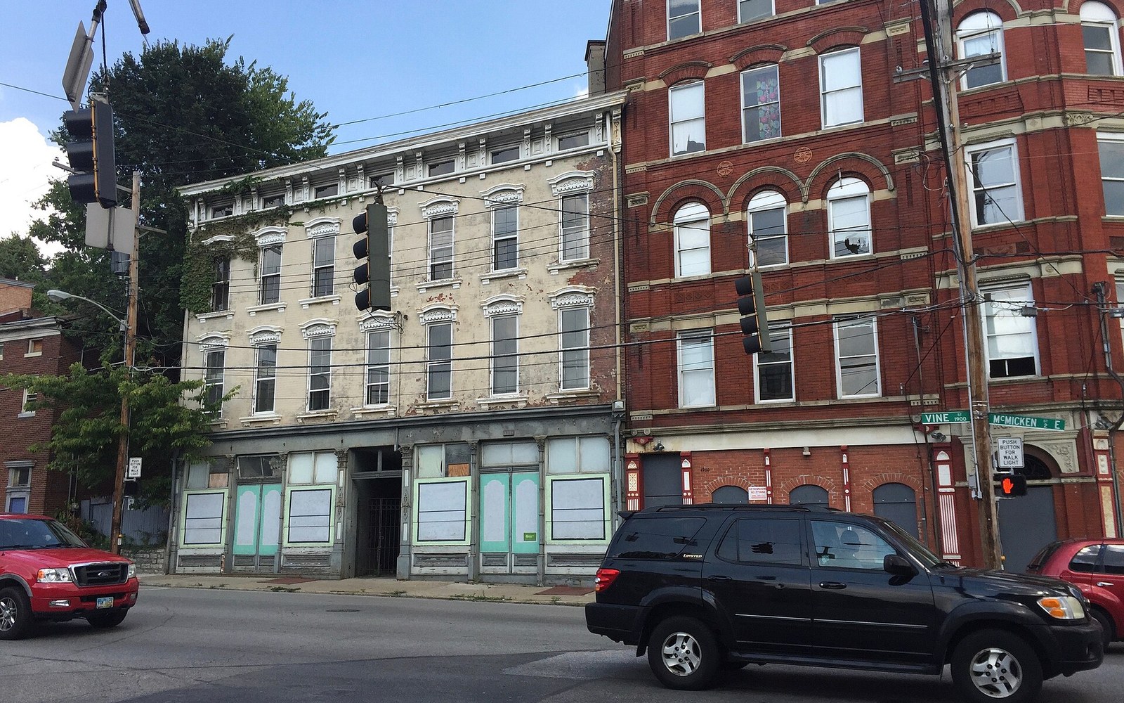 Vacant Italianate storefront buildings stand beside a red brick corner building at Vine and McMicken