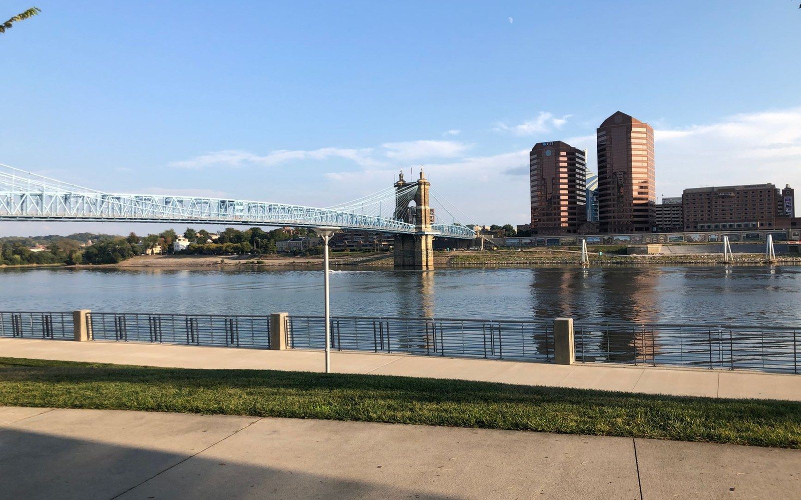 Suspension bridge spans a river toward a city skyline with high-rise buildings