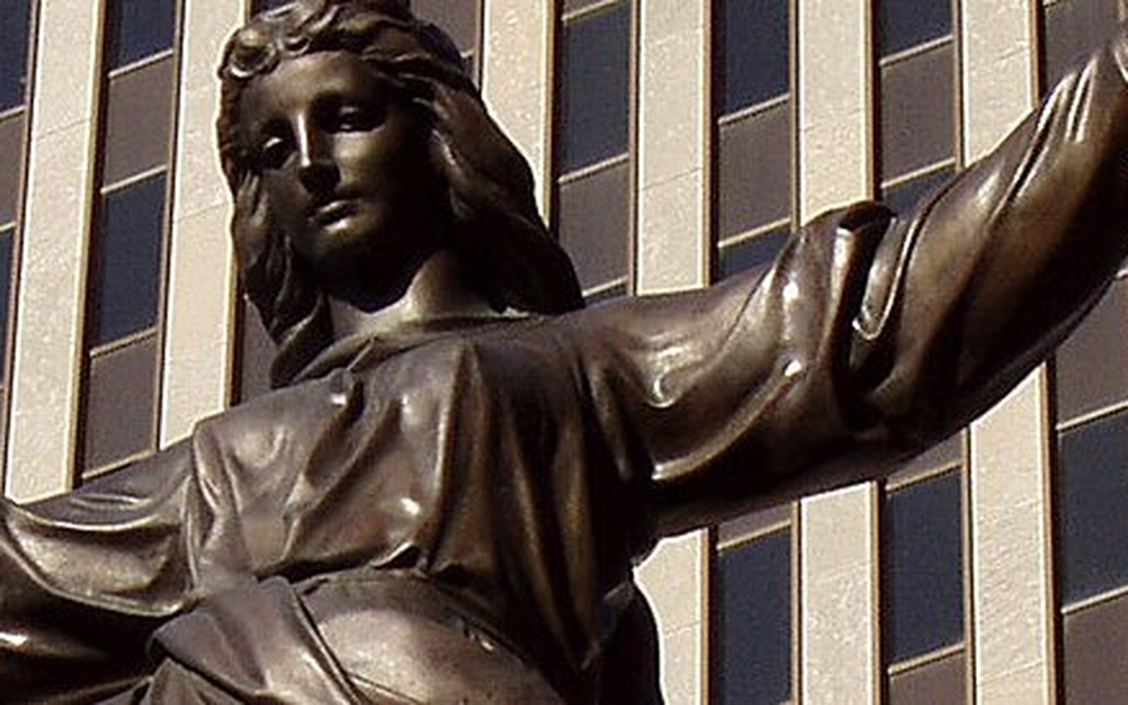 Bronze statue of a robed woman with outstretched arms in front of a glass office building